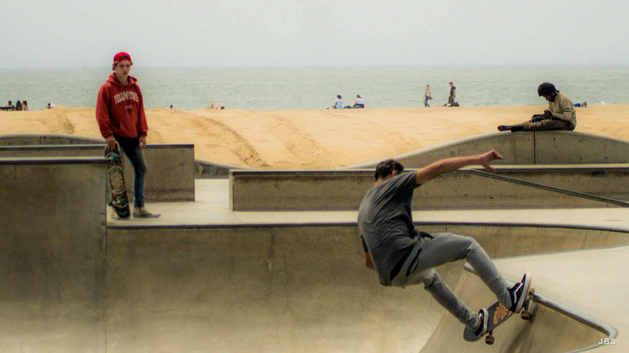 A skateboarder carving a concrete bowl beside the beach