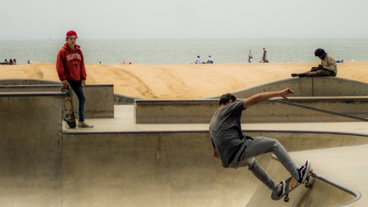 A skateboarder carving a concrete bowl beside the beach