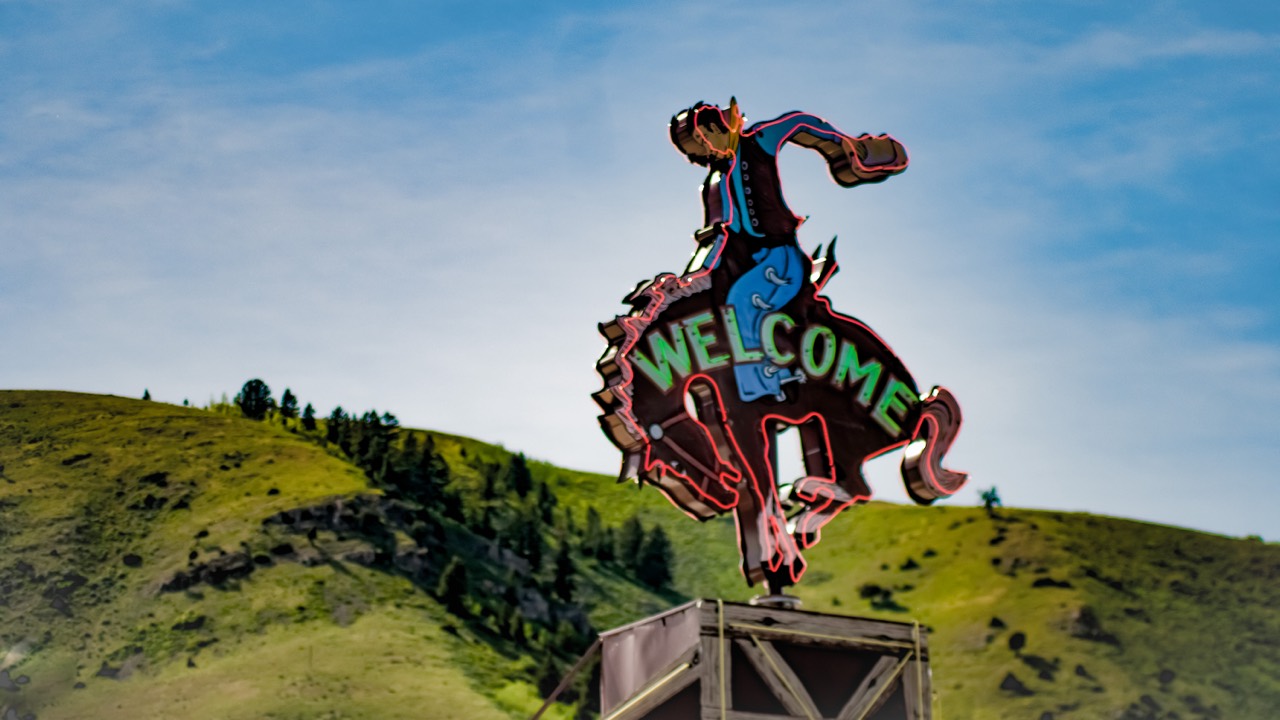 A bucking horse welcome sign against green hills and blue sky