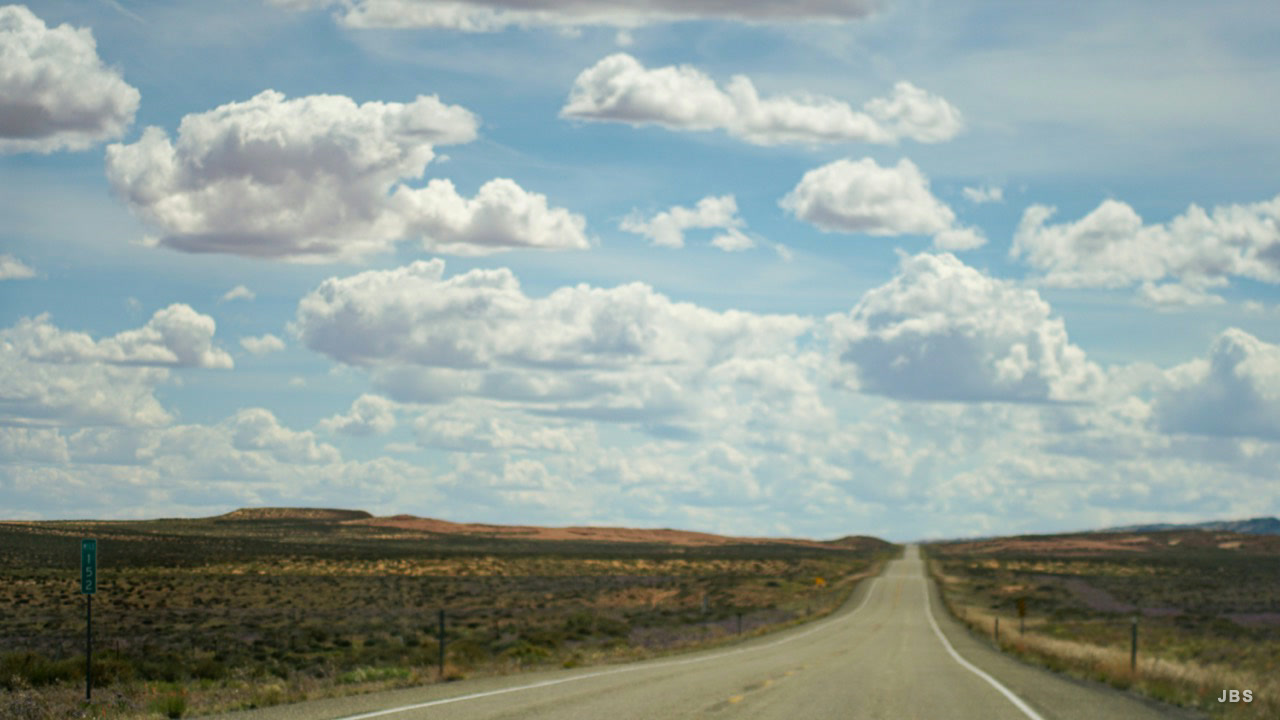 A straight highway running beneath a field of bright clouds