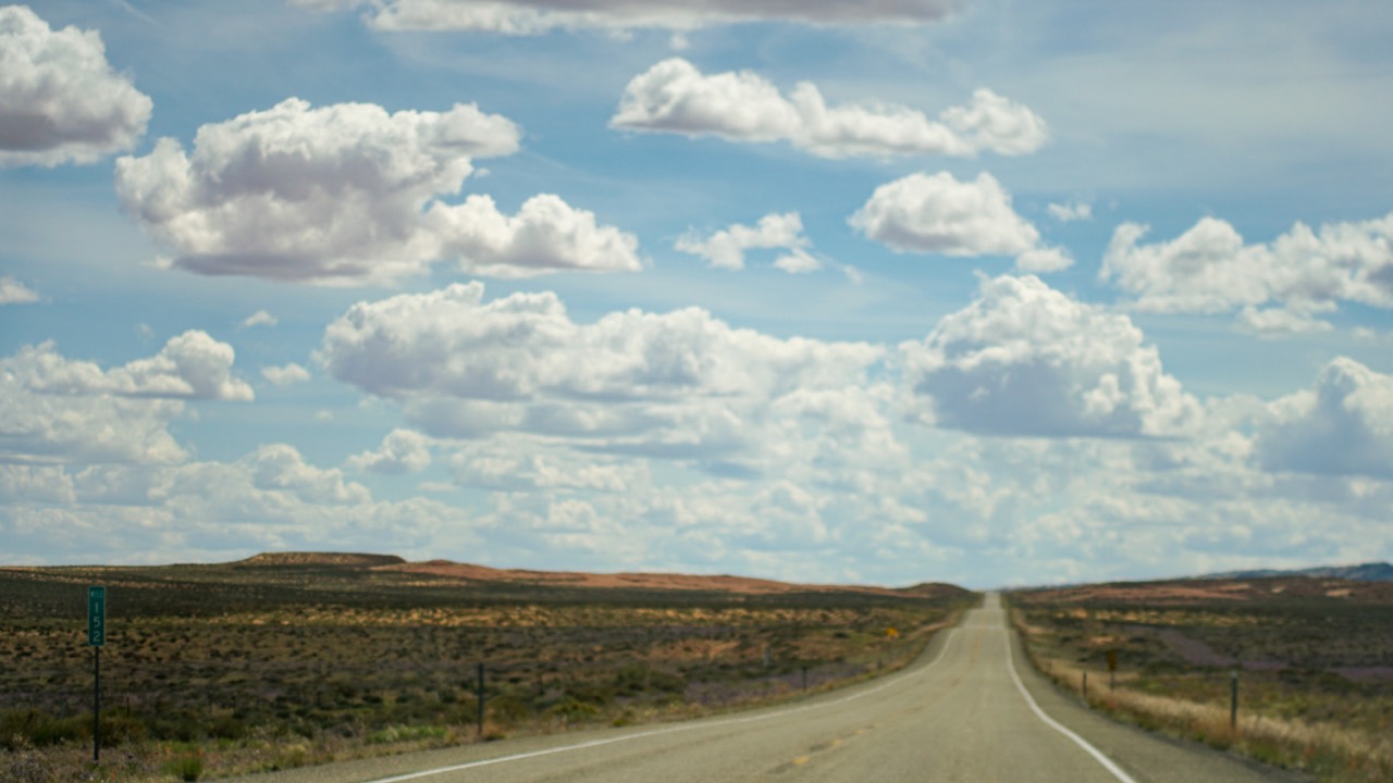 A straight highway running beneath a field of bright clouds