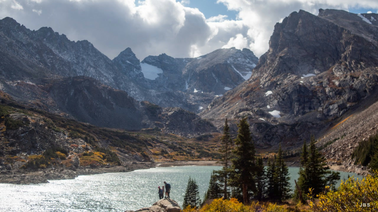 Hikers overlooking a bright alpine lake beneath rocky peaks