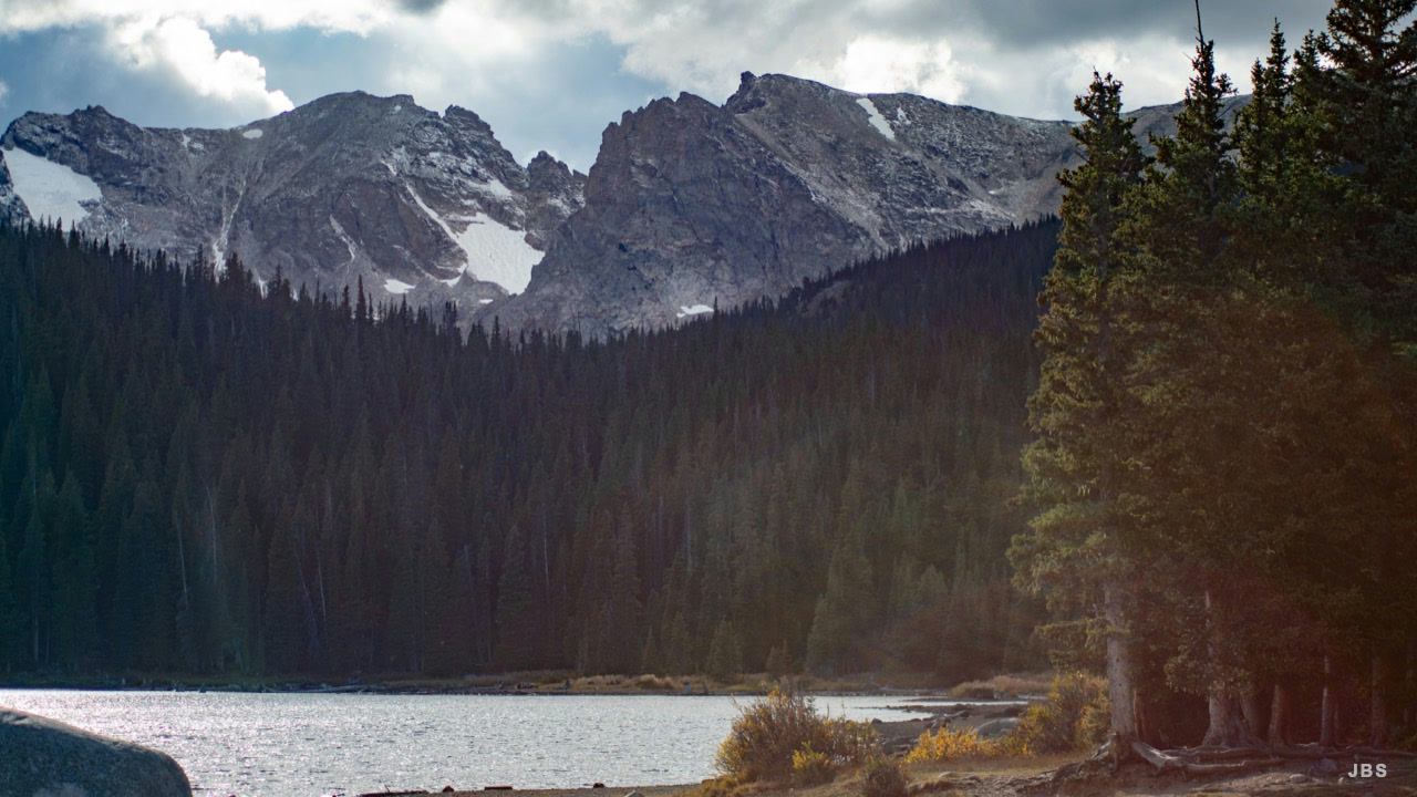 A mountain lake bordered by dense evergreens and snowy peaks