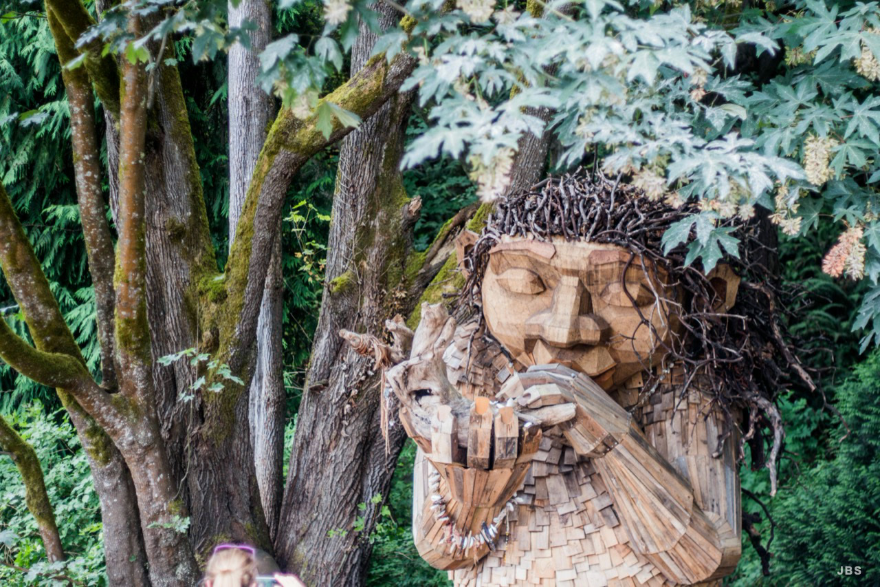 A wooden forest figure holding a small deer beneath maple leaves