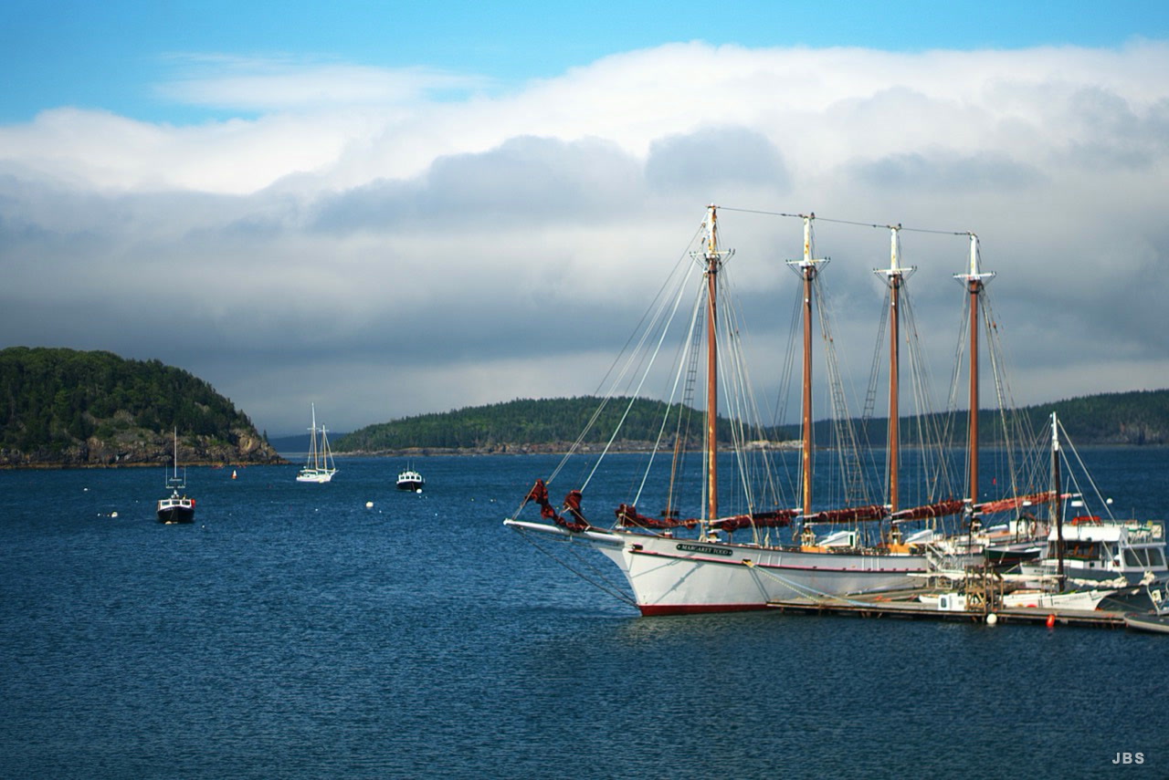 A four-masted schooner moored in a blue coastal harbor