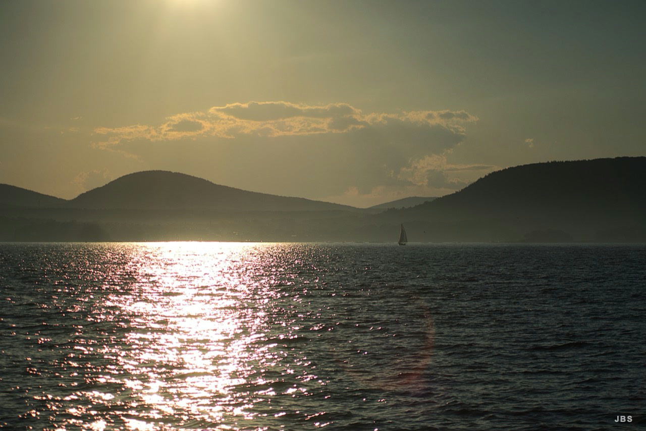 Sunset light crossing the sea toward a distant sailboat