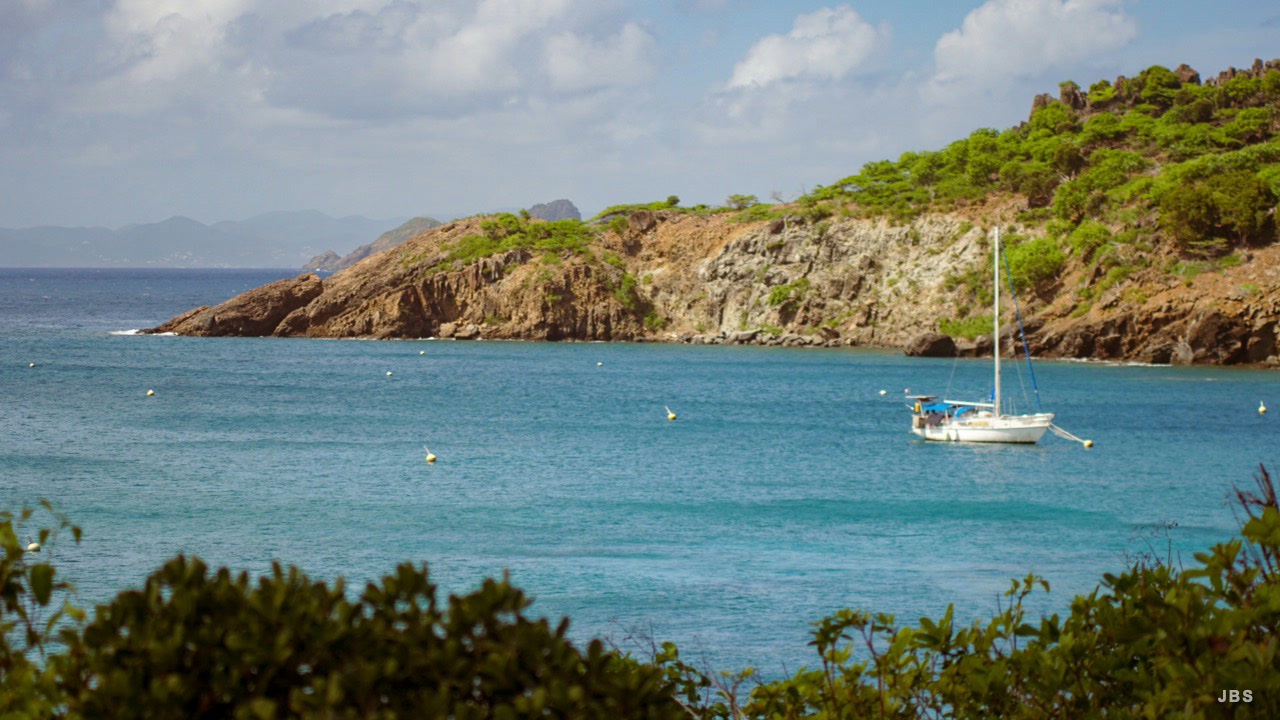A sailboat moored in a turquoise cove beneath rocky hills