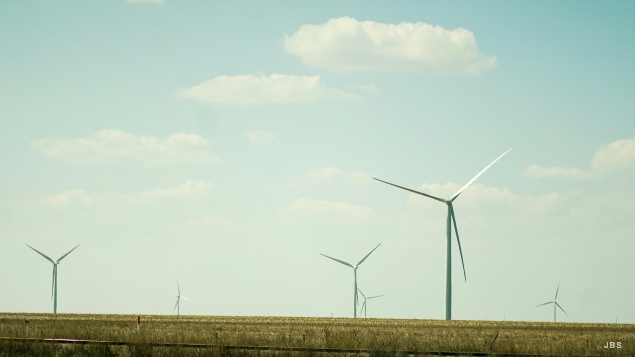 Wind turbines turning across an open grassland beneath soft clouds