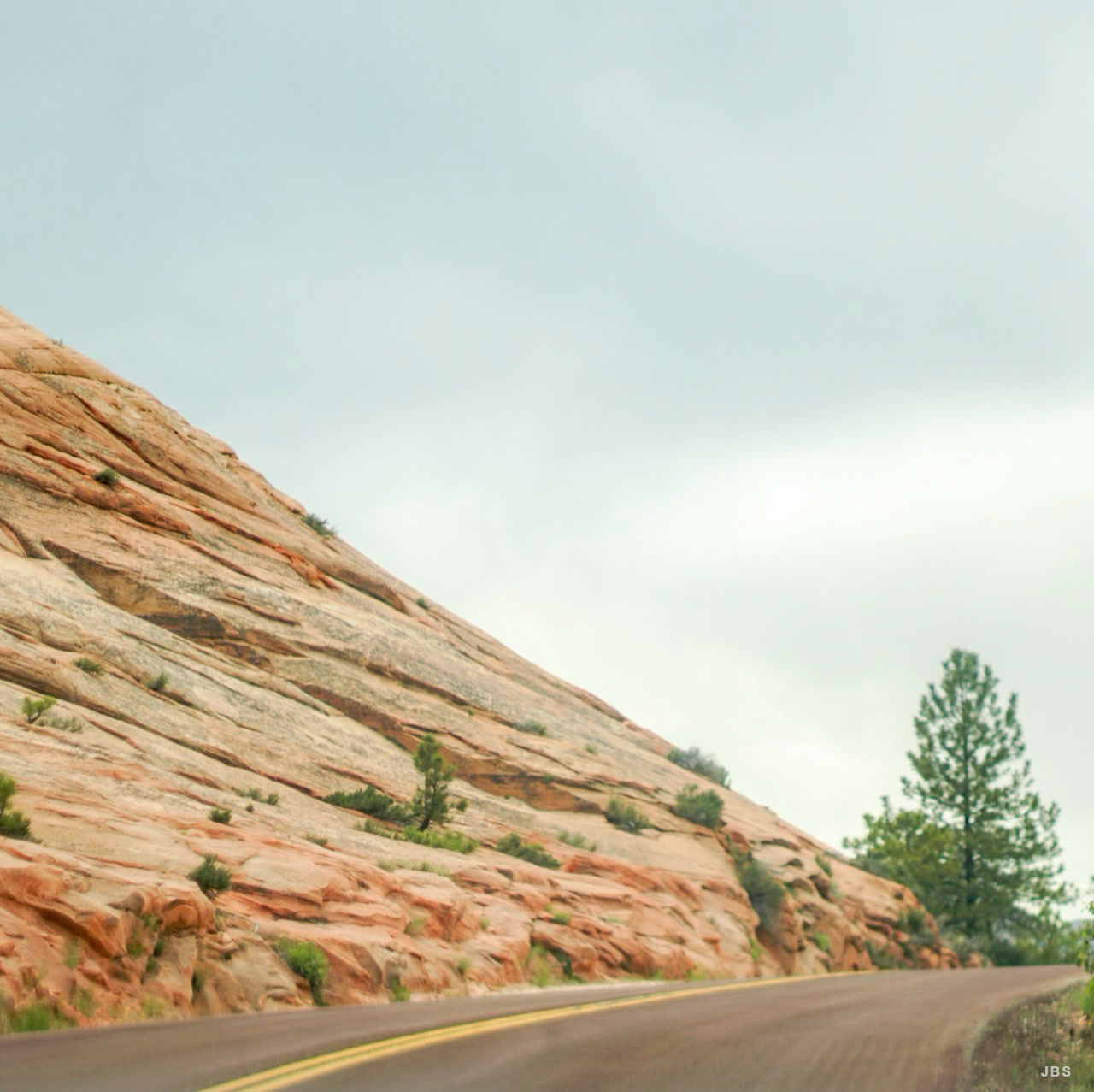 A quiet road curving past a broad red sandstone slope