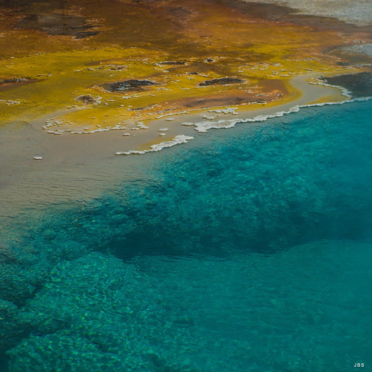 A vivid boundary of amber mineral earth and clear turquoise spring water