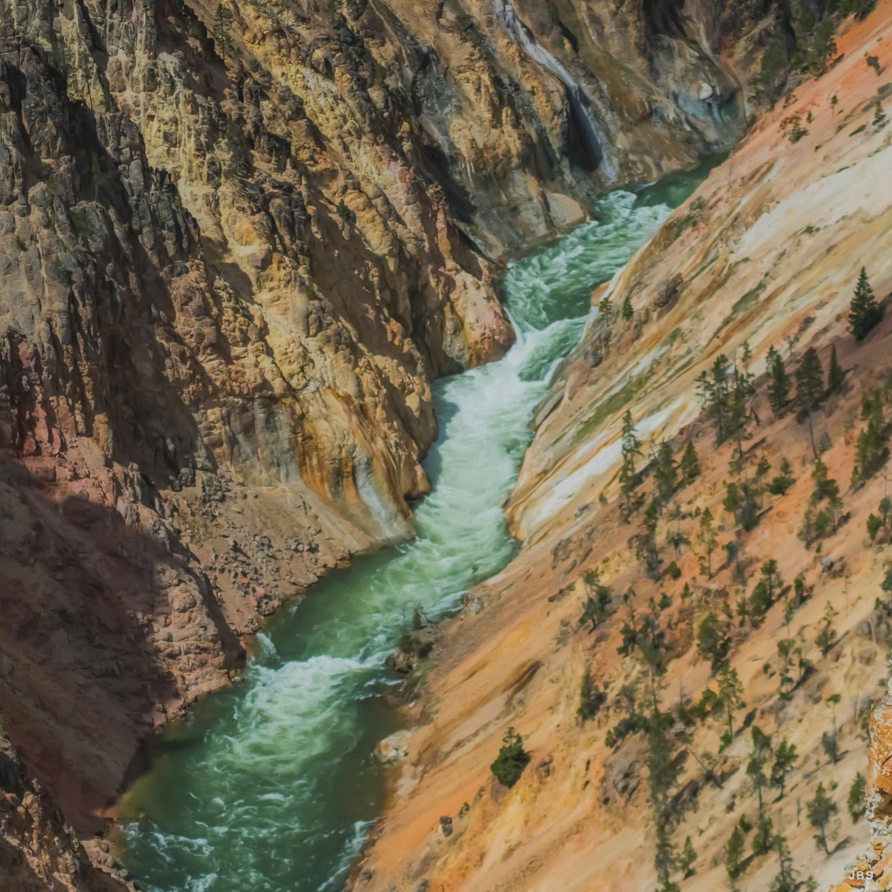 A green river rushing through steep ochre canyon walls