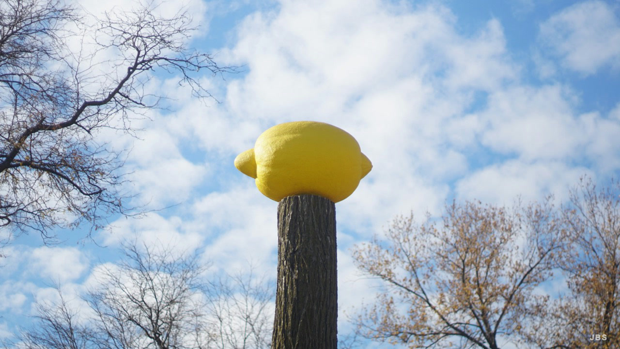 A giant yellow lemon perched on a tree trunk beneath a bright sky